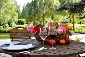 A wooden table set with a plate, cutlery, two wine glasses, and a wicker basket with flowers and apples.