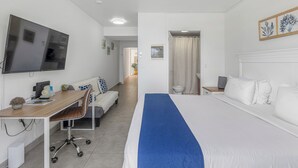 A hotel room with a bed, a desk with a chair, a television, and a bathroom visible through an open door.