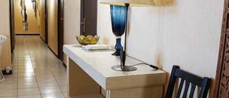 Un couloir d’hôtel avec un comptoir de réception, une chaise, une lampe, un tableau encadré et une porte.