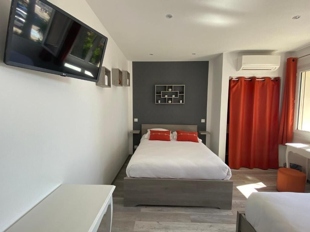 A modern hotel room with a bed, a TV mounted on the wall, a desk, and a window with curtains.