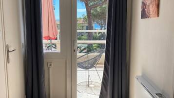 Een kamer met een deur die leidt naar een balkon, een stoel ernaar en een kleine ronde tafel.