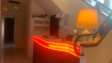 A reception desk with a red neon light, a staircase, and a wall with various notices.