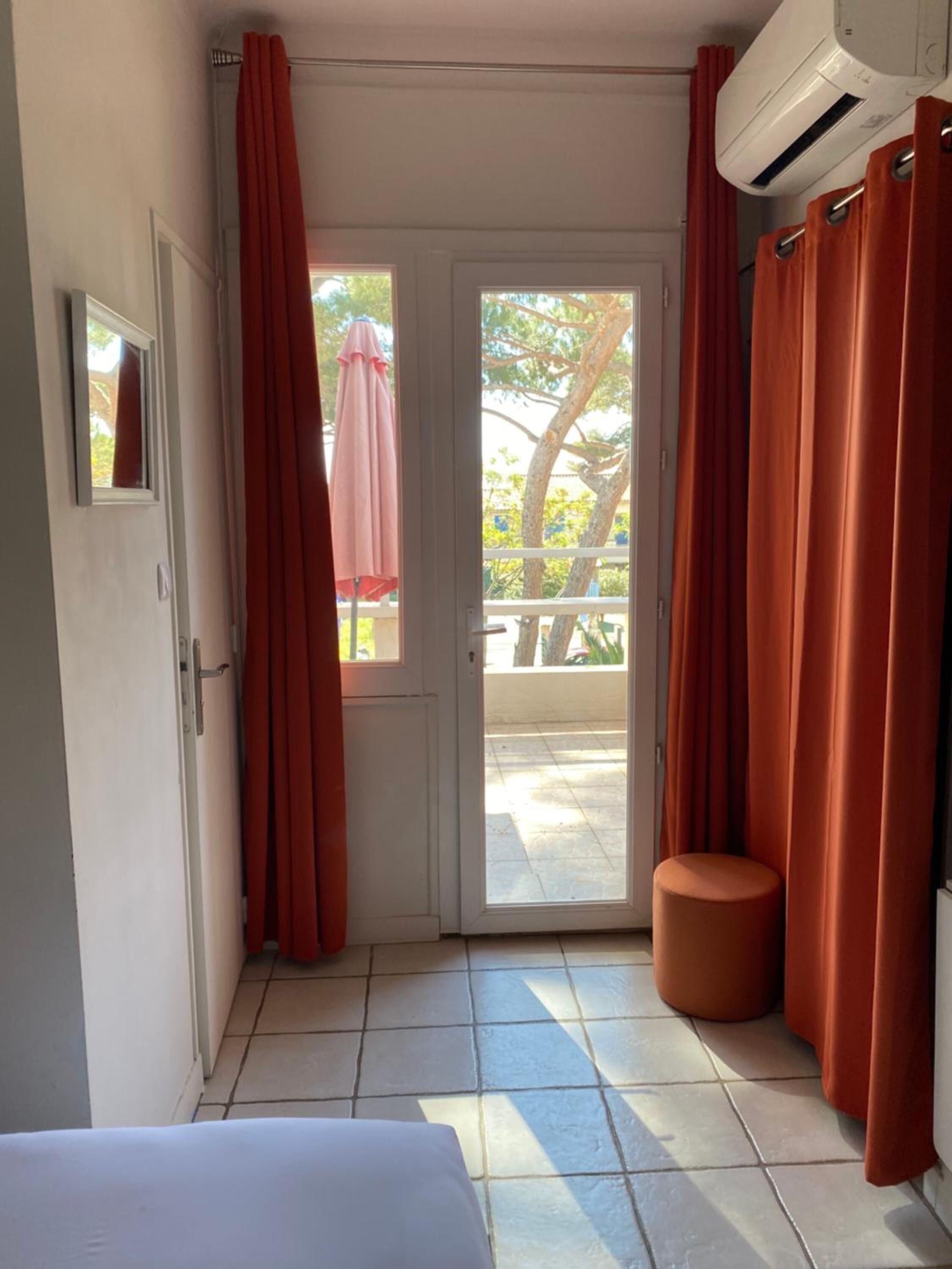 A hotel room with a sliding glass door leading to an outdoor area, a small round stool, and a ceiling-mounted air conditioning unit.
