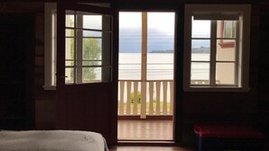 Ein Zimmer mit einem Bett, Holzboden und zwei Fenstern mit Blick auf ein Gewässer.