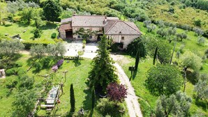 Une maison en pierre, avec un toit de tuiles, entourée d’une végétation luxuriante et d’oliviers.