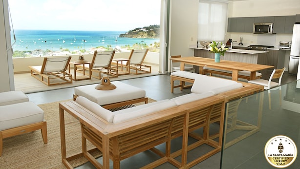 Een moderne villa met een balkon met uitzicht op een strand, een keuken met roestvrijstalen apparatuur en een eethoek met houten meubels.