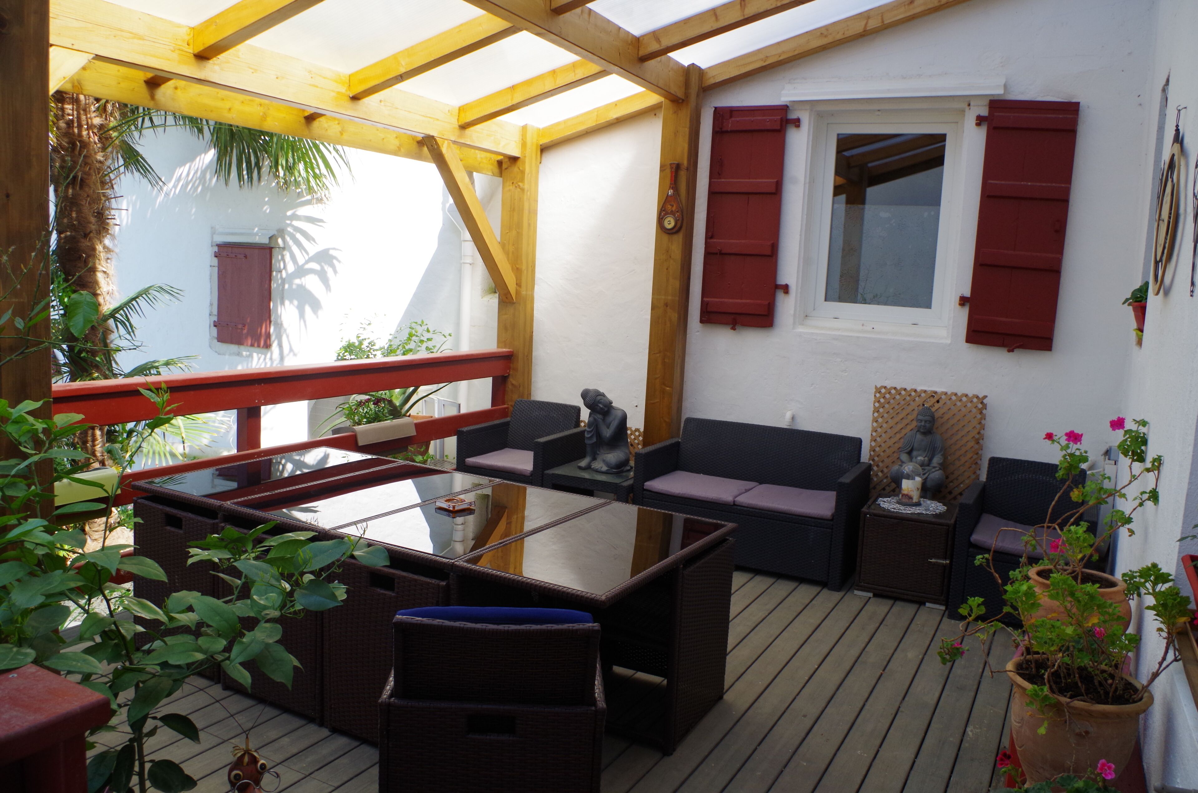 An outdoor patio with a glass-top table, wicker furniture, and red shutters on the windows.