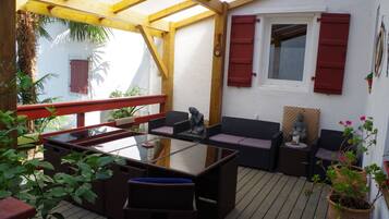 An outdoor patio with a glass-top table, wicker furniture, and red shutters on the windows.