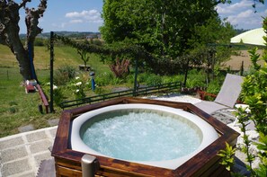 Ein Whirlpool, umgeben von einer Holzterrasse, mit Blick auf ein Wiesfeld und Bäume im Hintergrund.