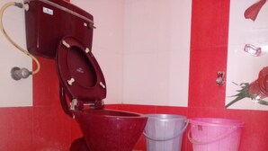 Un baño con un inodoro rojo, un cubo gris y un cubo rosa.