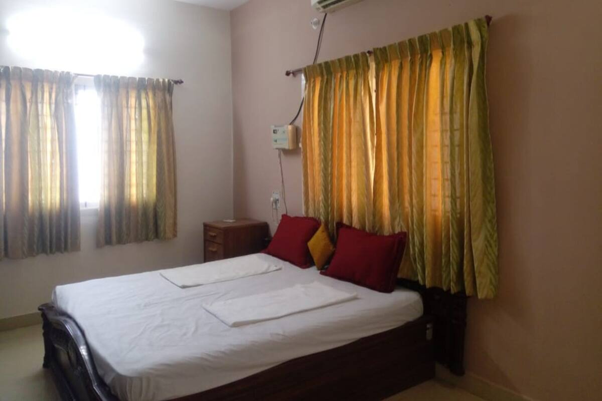 A bedroom with a bed, an air conditioner, a nightstand, and curtains.