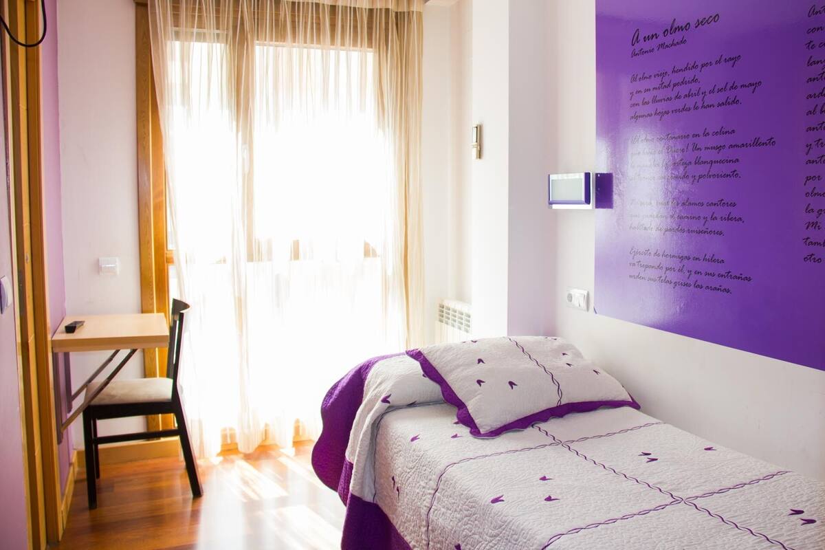 A bedroom with a bed, a desk, and a window with curtains.
