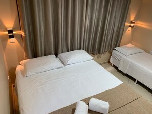 A hotel room with a large bed, two bedside tables, and a smaller bed. - Praia do Forte Suites (Mata de São João)