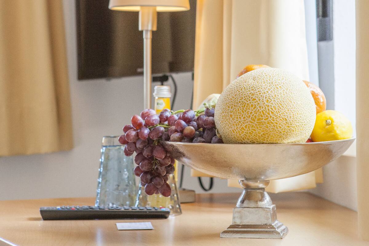 A table with a fruit bowl containing grapes, a melon, and a lemon, a remote control, and a glass of water.