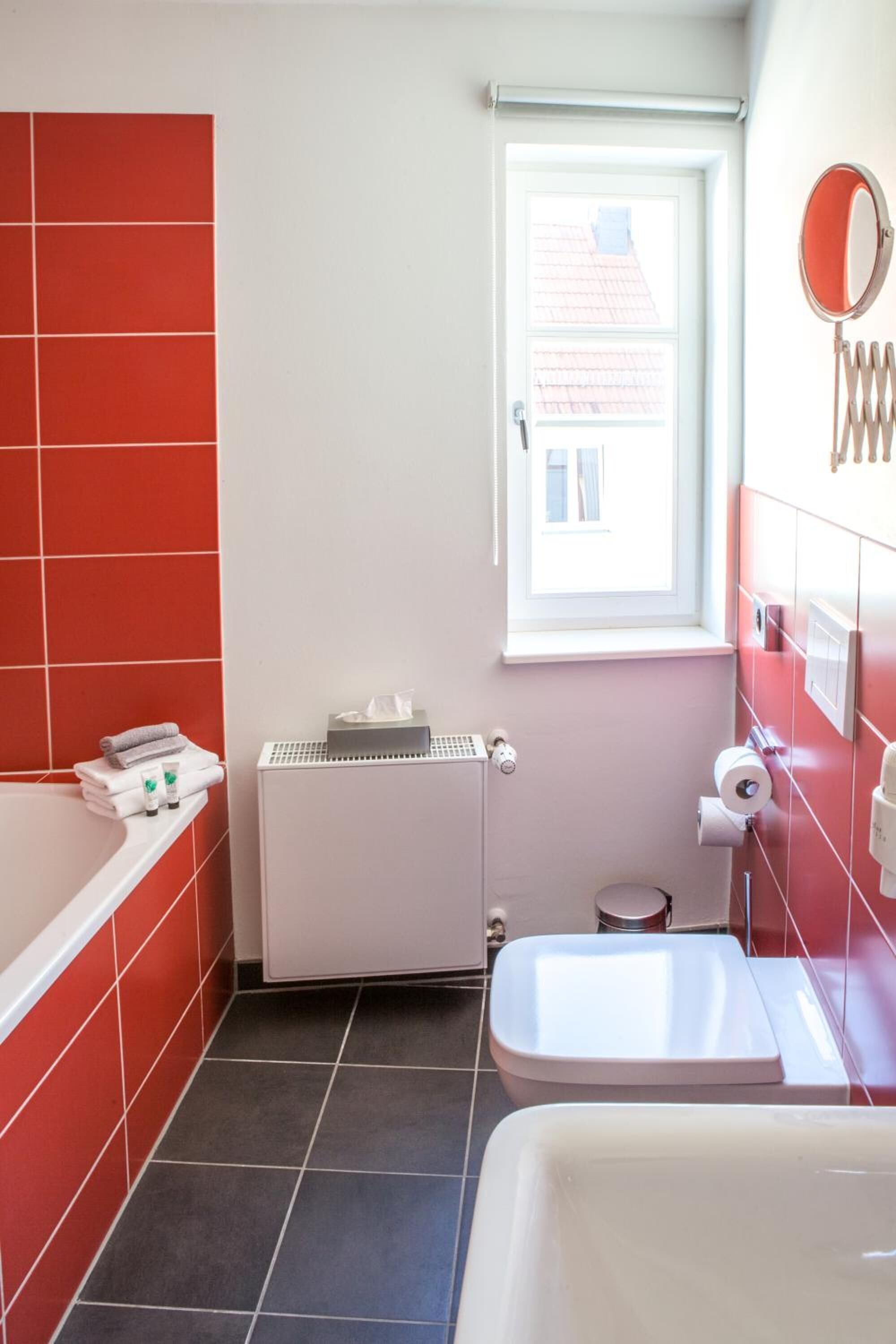 A bathroom with red and white tiles, a white radiator, a window, a toilet, and a sink.