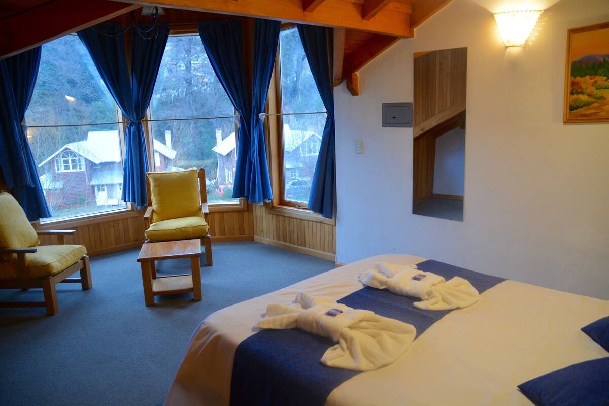 A hotel room with a bed, two chairs, a window with curtains, and a painting on the wall.