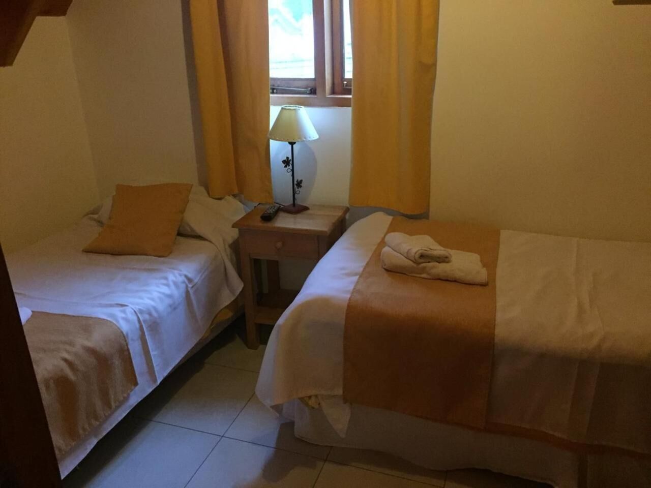 A bedroom with two single beds, a nightstand with a lamp, and a window with curtains.