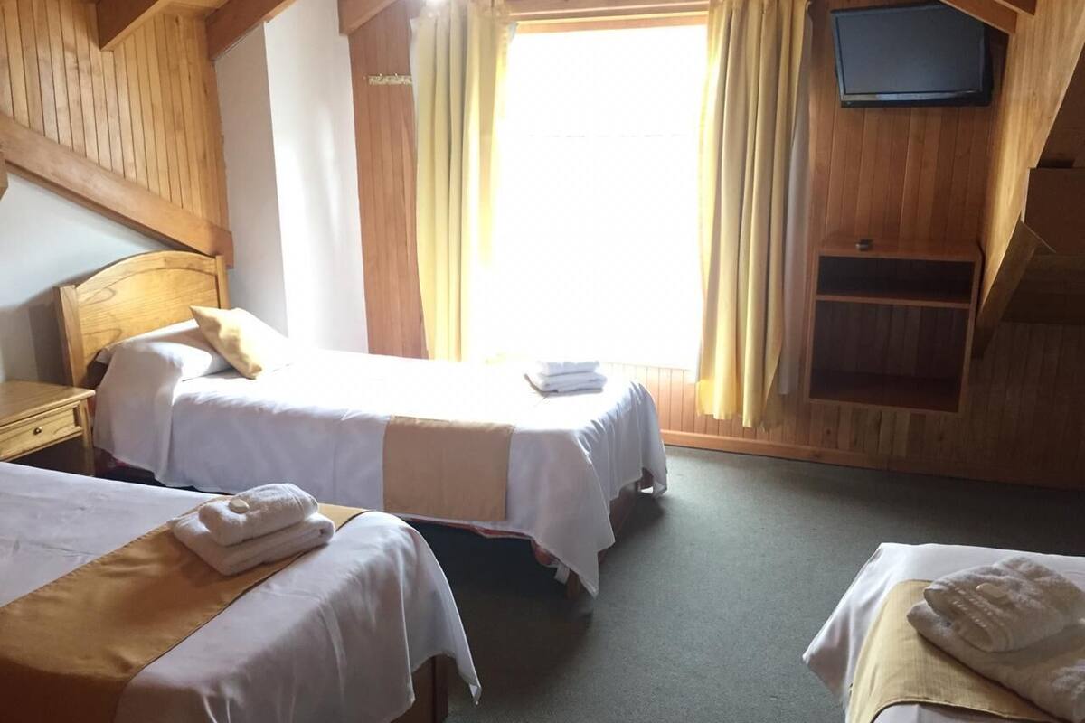 A room with two beds, a television mounted on the wall, and a wooden ceiling.