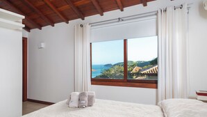Ein Schlafzimmer mit großem Fenster, einem Bett und Blick auf eine Küstenlandschaft.