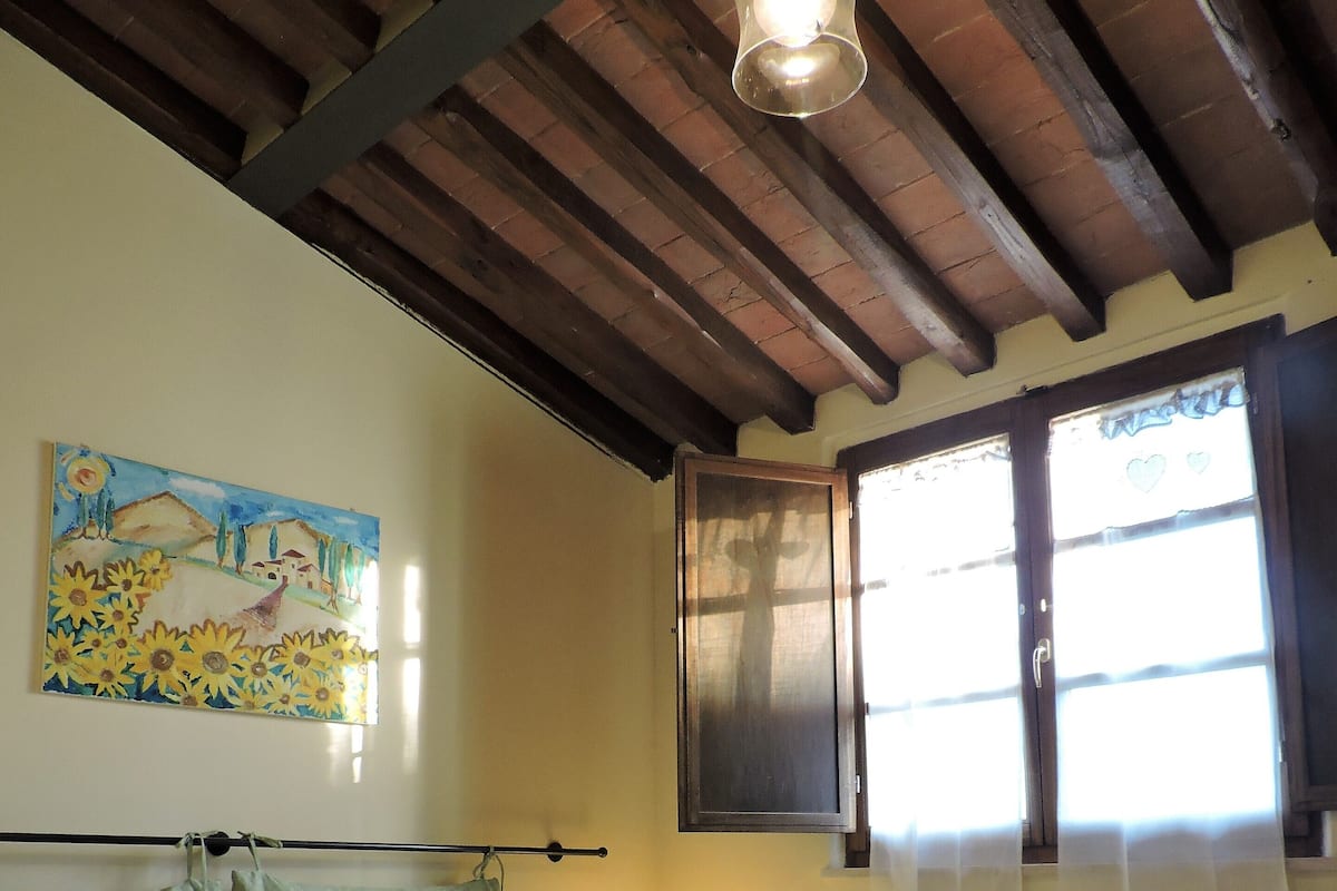 Ein Schlafzimmer mit zwei Betten, einem Bild an der Wand, einem Fenster mit Vorhängen und einer Pendelleuchte.