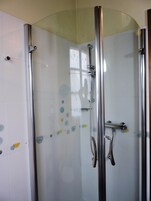 Ducha con cerramiento de vidrio, detalles cromados y pared de azulejos.