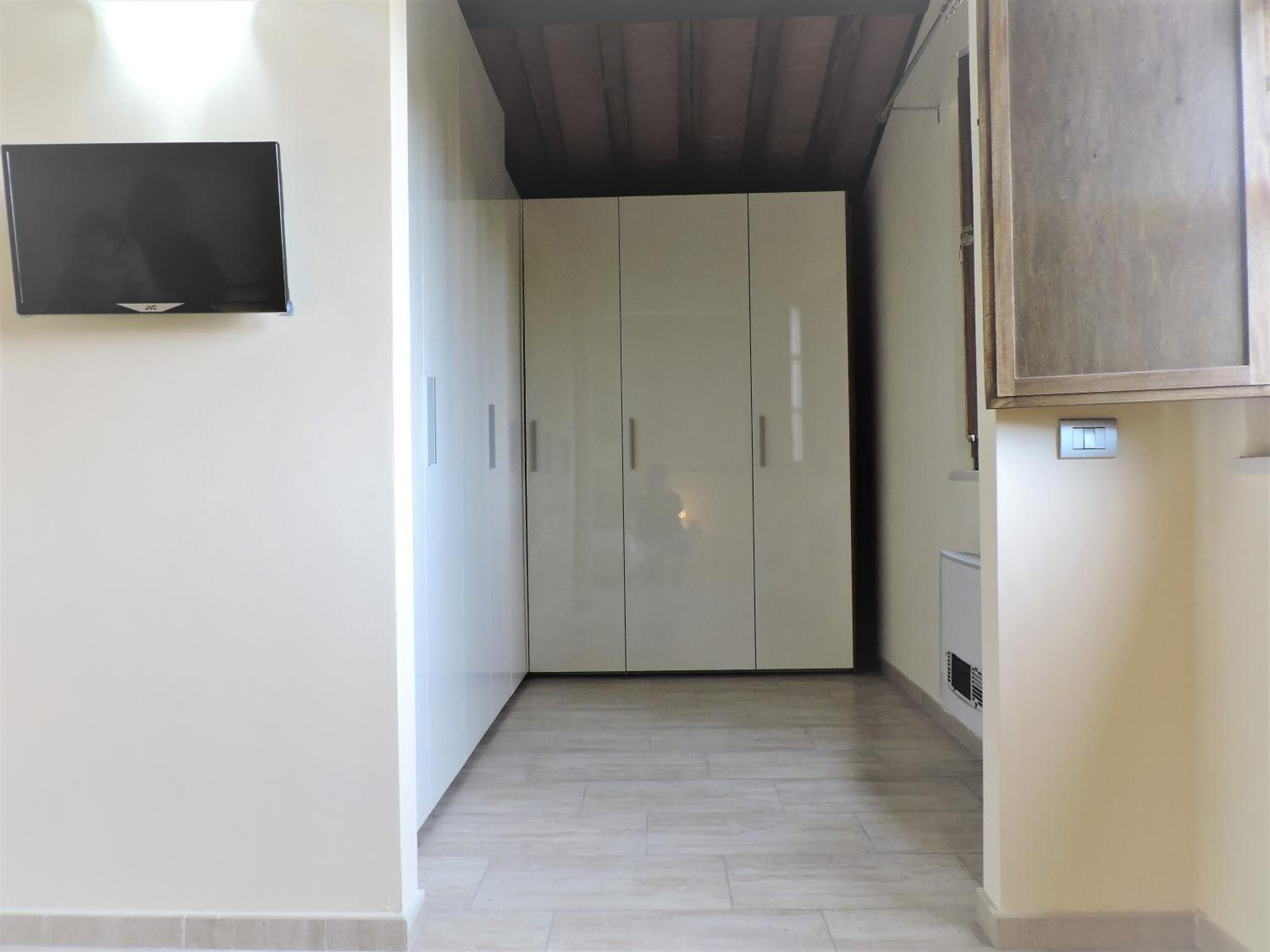 A hallway with a wardrobe, a television mounted on the wall, and a light switch on the wall.