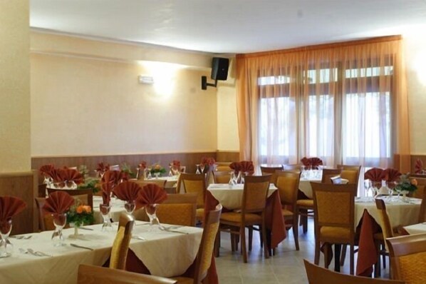 Zona pranzo con tavoli apparecchiati, sedie e un'ampia finestra con tende.