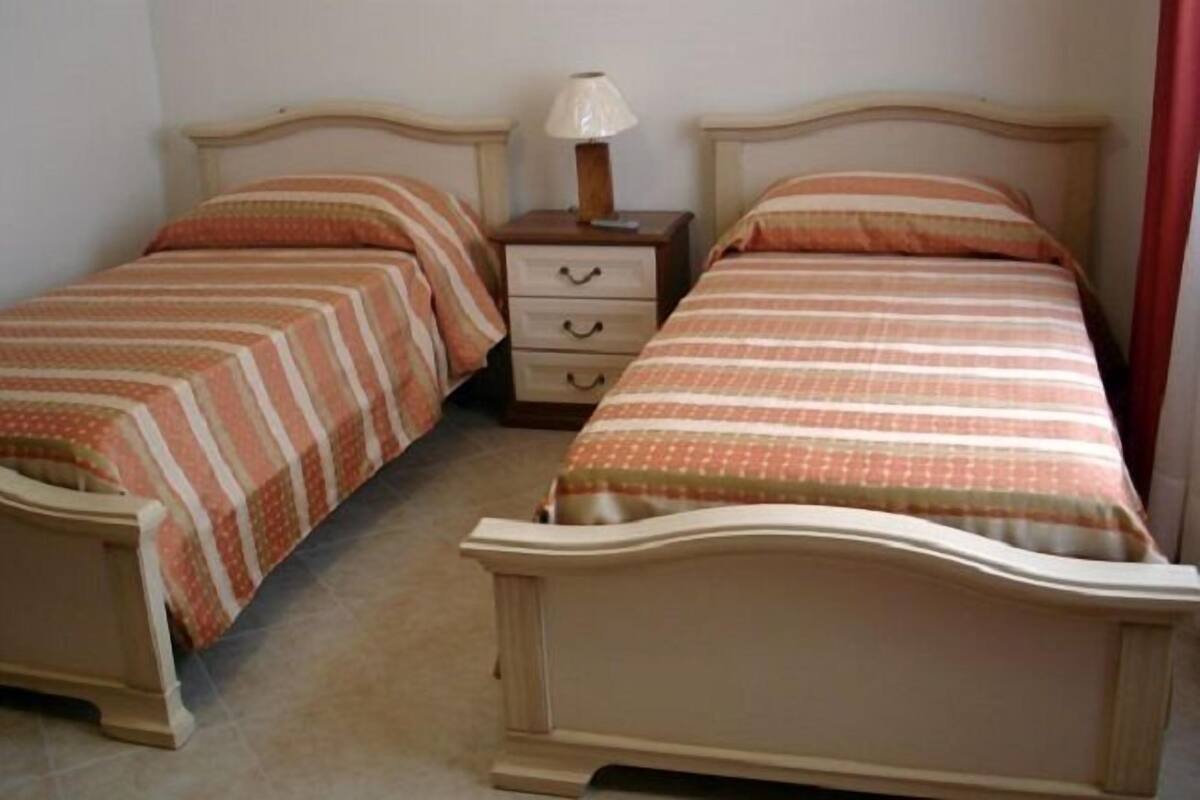 A room with two single beds, each with a wooden headboard and a matching nightstand with a lamp.
