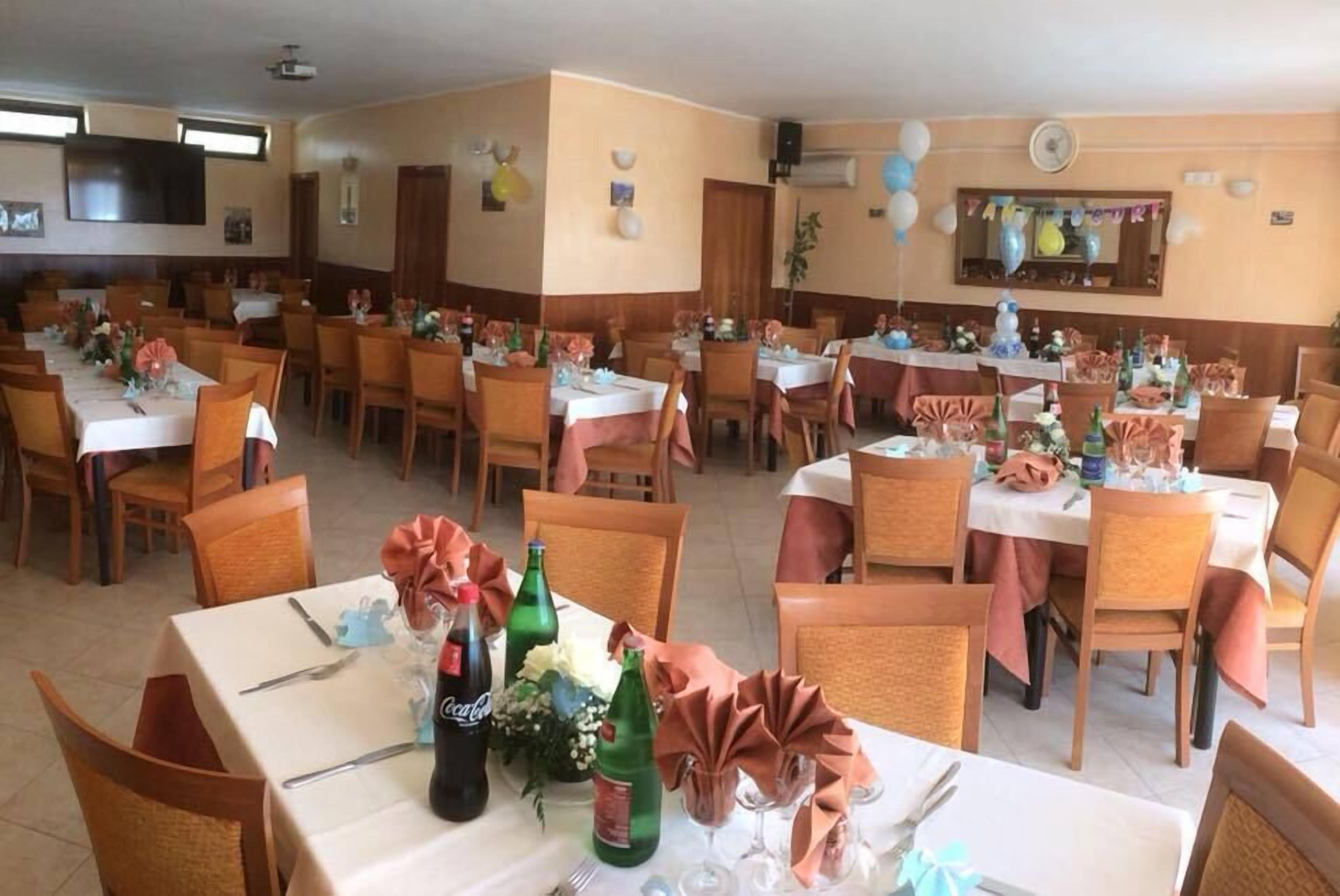 Une salle à manger avec plusieurs tables dressées pour une fête, décorée de ballons et de fleurs.