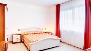 Un dormitorio con cama, mesitas de noche y una ventana con cortinas.