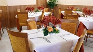 Un salón de banquetes con mesas redondas, cada una cubierta con mantel blanco, sillas doradas y aros para servilletas rojos.