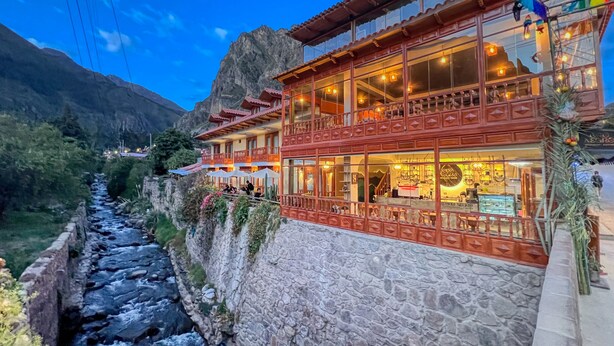 A traditional building with balconies, a stone wall, and a river. - Sol Ollantay Exclusive Hotel (Ollantaytambo)
