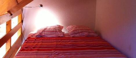 A single bed in a room with wooden beams and a sloped ceiling, a wall-mounted light, and a poster.