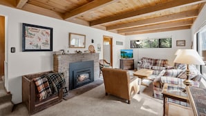 Un salon chaleureux avec une cheminée, des meubles à motifs écossais et des poutres en bois au plafond.