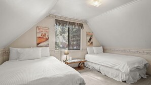 Une chambre avec deux lits, une fenêtre donnant sur des arbres et une lampe sur une petite table.