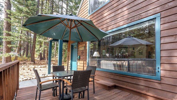 Une terrasse en bois avec une table et des chaises, un parasol et une grande fenêtre.