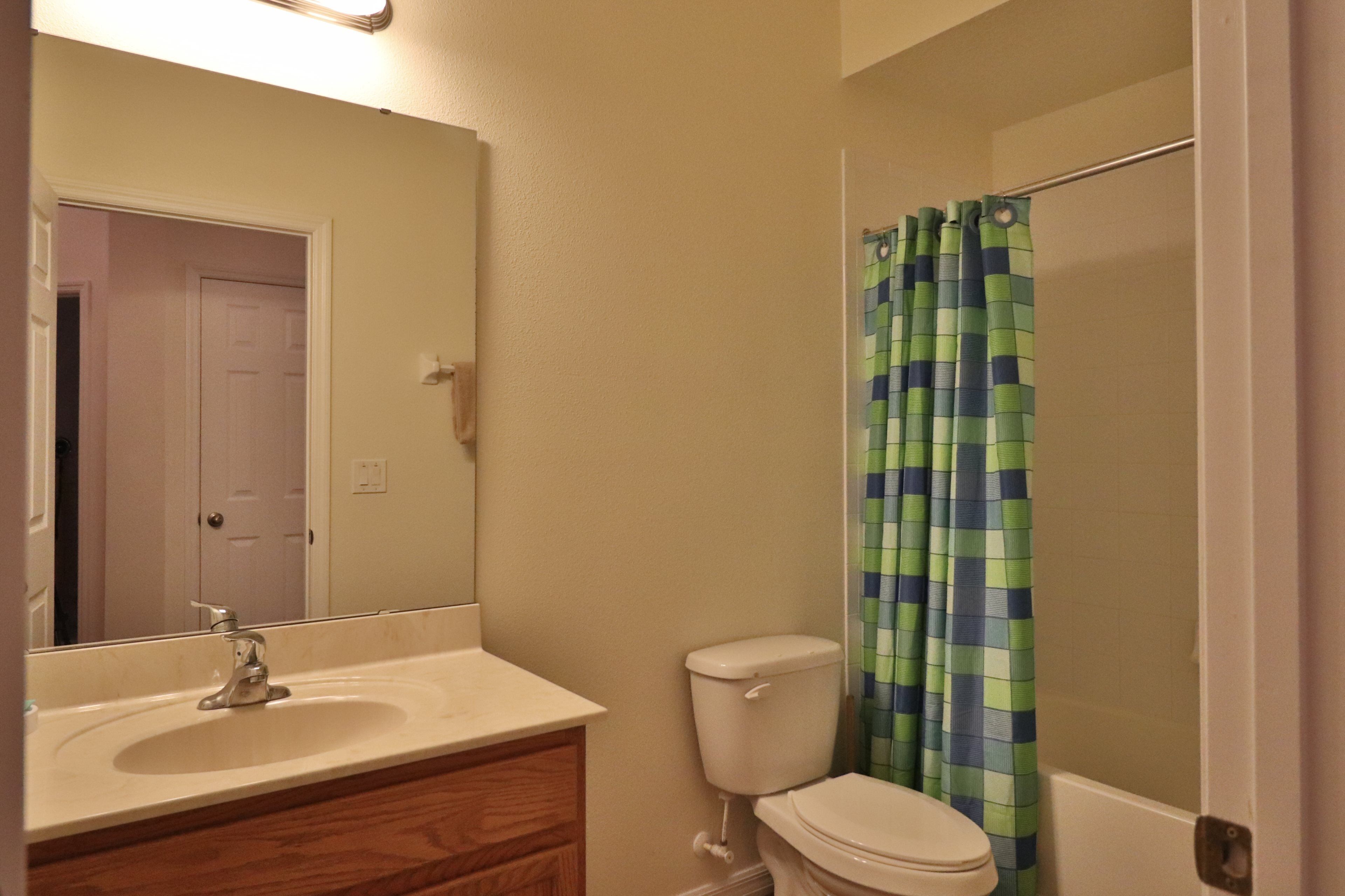 A bathroom with a sink, mirror, toilet, and shower curtain.