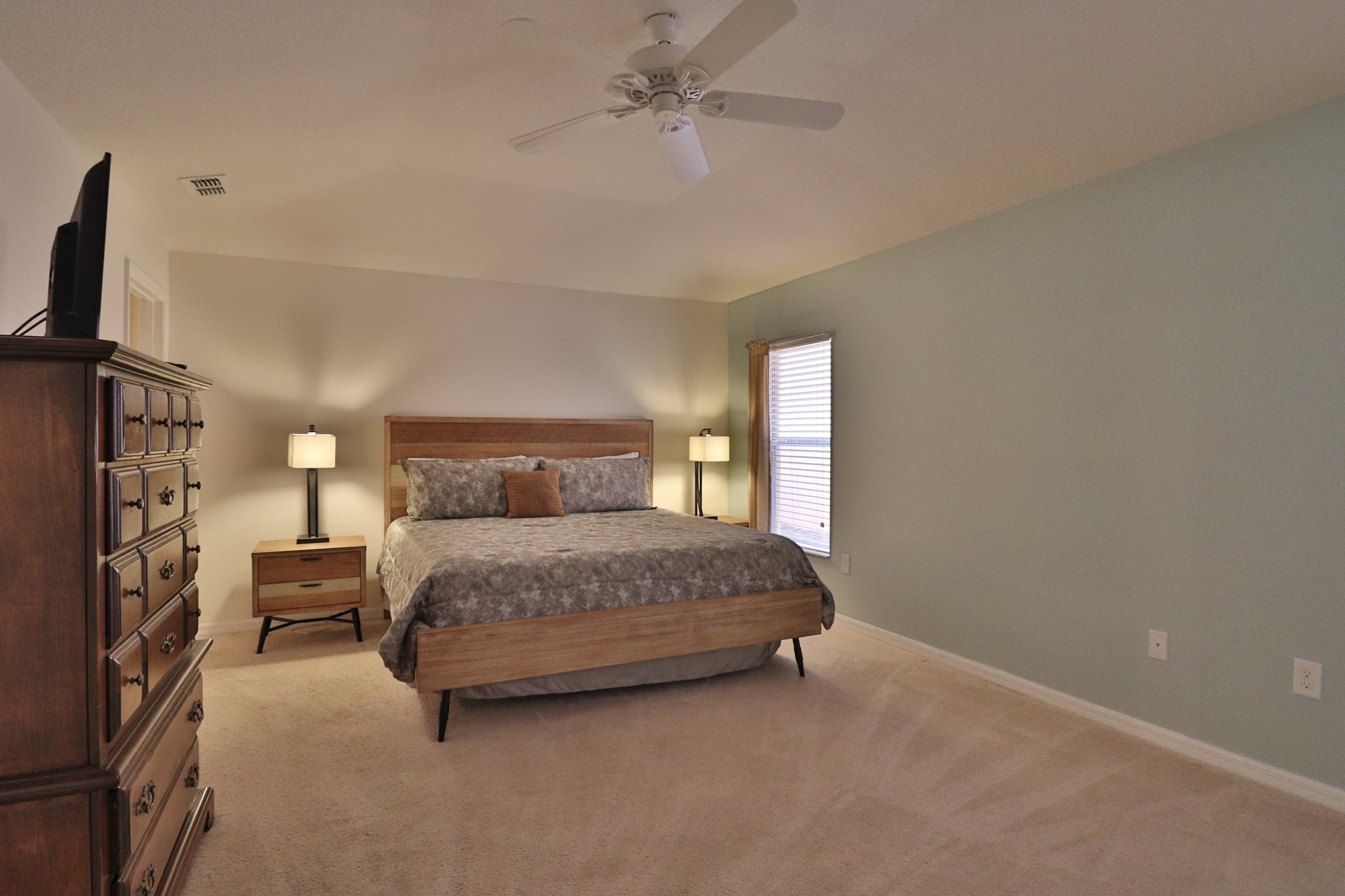 A bedroom with a bed, dresser, nightstands, lamps, and a ceiling fan.