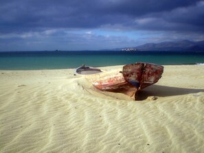 A boat on a sandy beach with a clear view of the ocean and distant mountains.