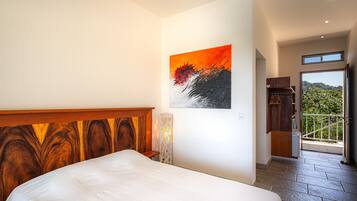 A bedroom with a wooden headboard, a painting on the wall, and a view of the outdoors through a door.
