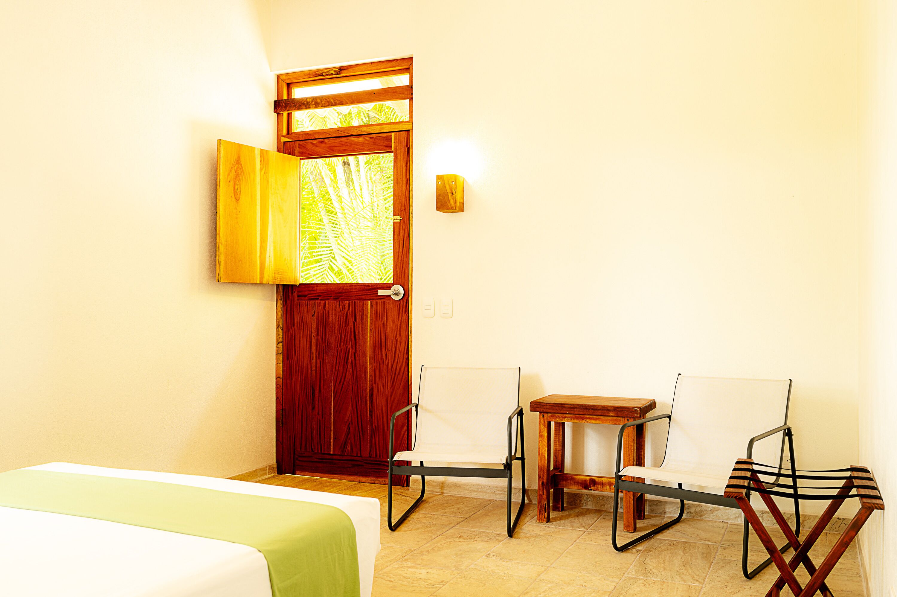 Une pièce avec un lit, une porte en bois, une petite table et deux chaises.