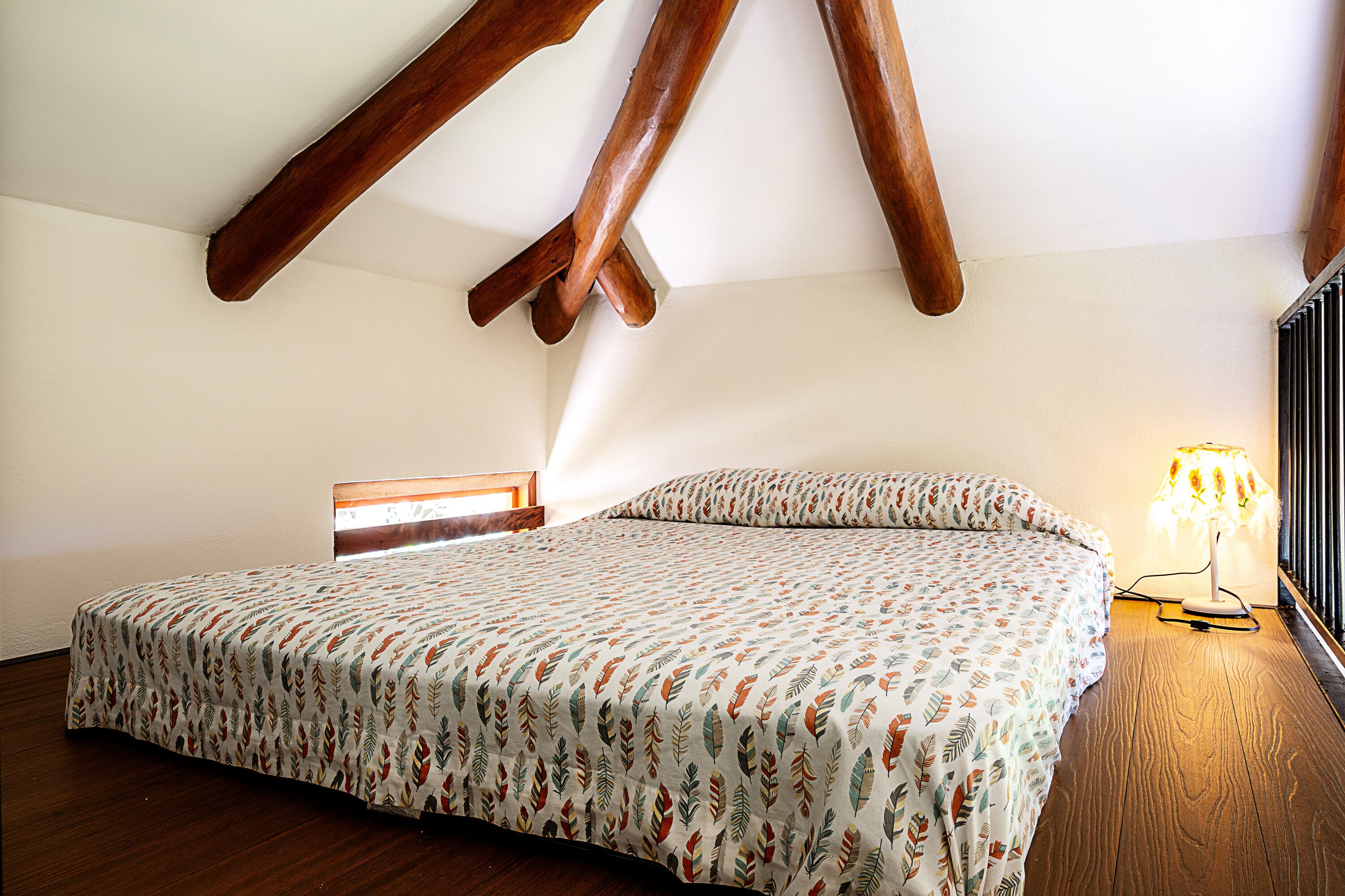 A bedroom with a bed, wooden beams, a nightstand, and a lamp.