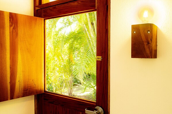 A wooden door with a window revealing palm trees outside.
