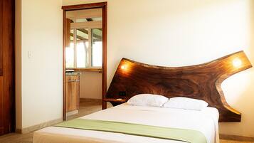 Un dormitorio con cabecera de madera, cama con ropa de cama blanca, manta verde y mesita de noche de madera.