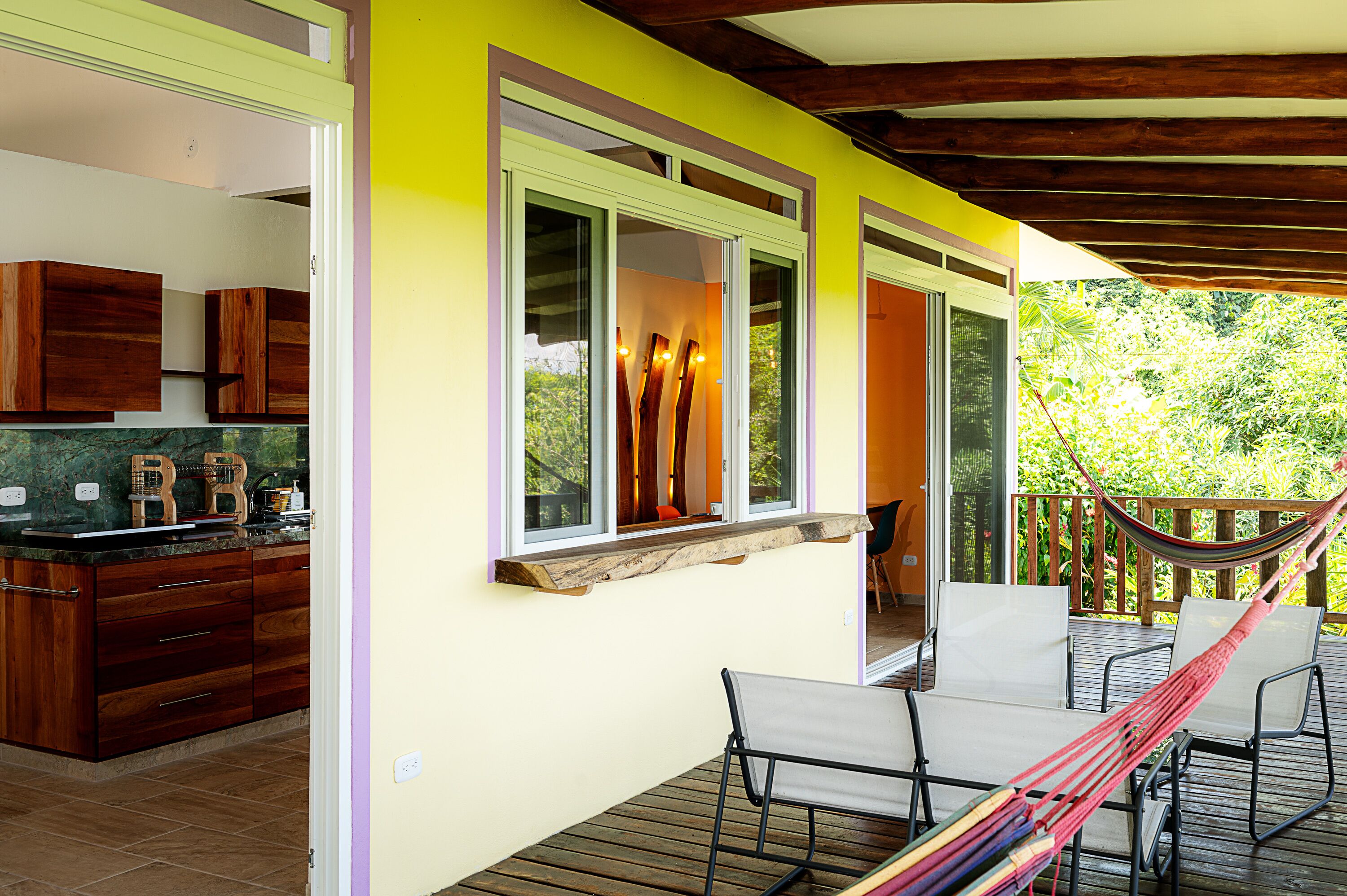 A bright yellow exterior wall with a wooden deck, a hammock, and a dining area with chairs and a table.