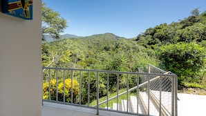 A balcony with a metal railing overlooking a lush, green forested area with a mountain in the background. - Casa Laureles (Bejuco)