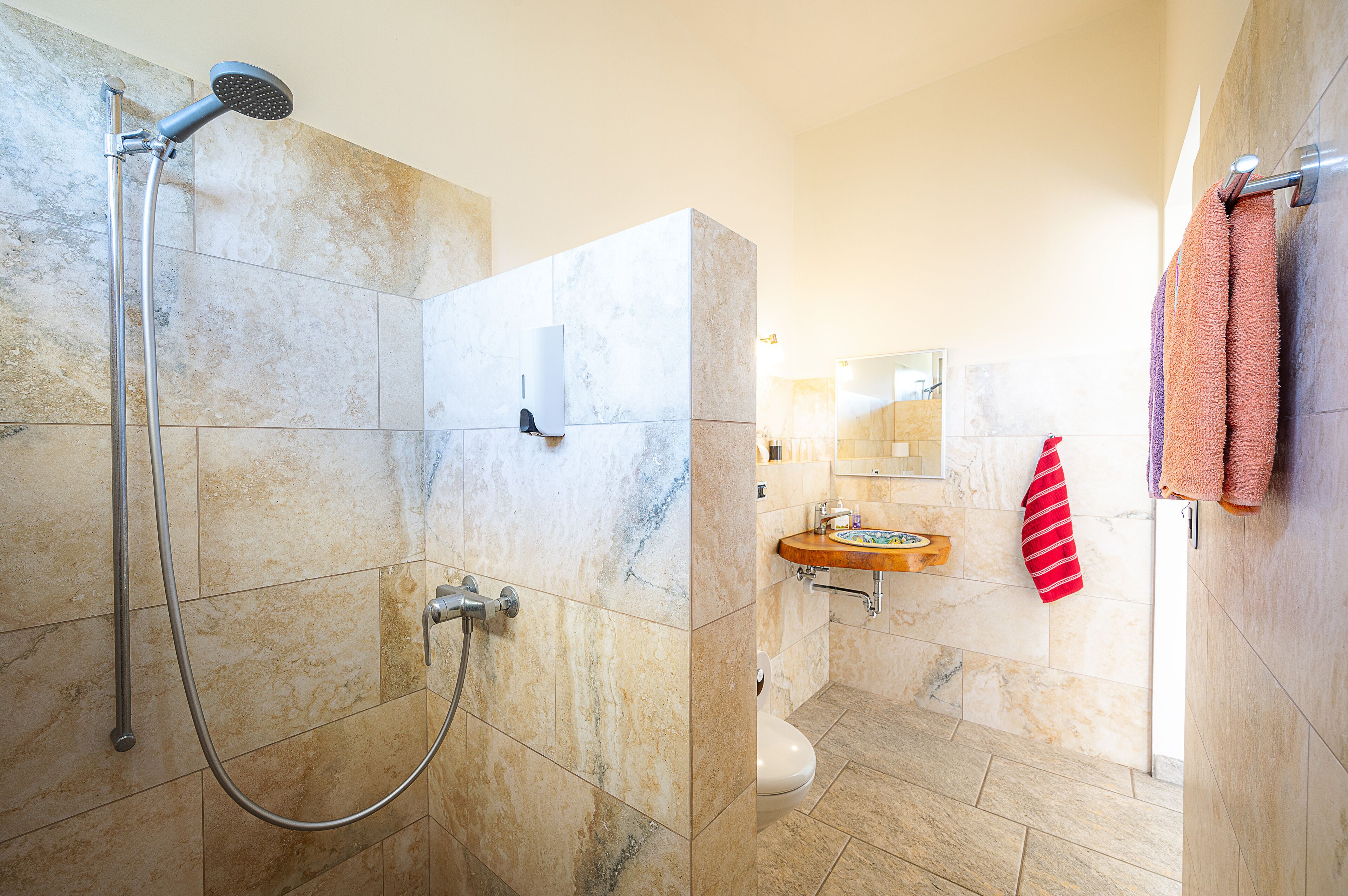 Baño con ducha, inodoro, lavamanos y perchero para toallas.