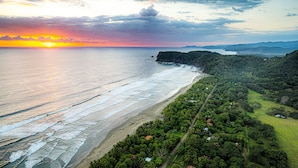 A coastal landscape with a beach, forested hills, and a sunset. - Casa Laureles (Bejuco)