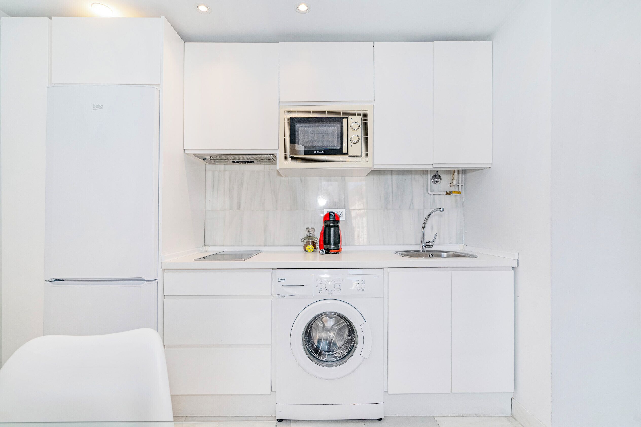 A compact kitchen with a microwave, coffee maker, sink, and washing machine.