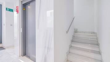 Un interior moderno con una escalera de mármol, un ascensor cerrado y señalización direccional.